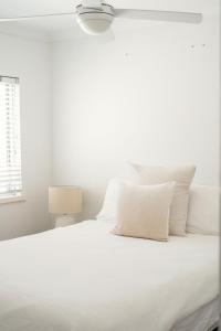 Cottesloe Beach View Apartments #11 في بيرث: سرير ابيض مع مخدات بيضاء ومصباح