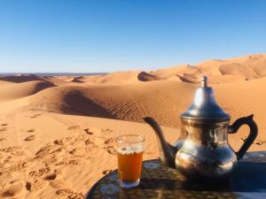 a tea kettle and a glass of beer in the desert at Desert Bird Camp in Merzouga