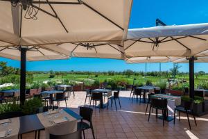 un restaurante con mesas, sillas y sombrillas en Isola di Albarella Golf Hotel en Isola Albarella