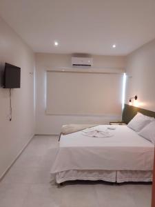 1 dormitorio con 1 cama blanca y TV en la pared en Pousada Primavera en Parnaíba