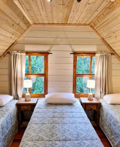 two beds in a room with two windows at Cabana Mirim Estalagem Rural in Gramado