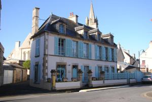 um edifício antigo com persianas azuis numa rua em Chambres Chez Mounie em Arromanches-les-Bains