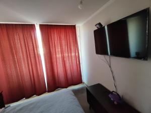 a bedroom with a tv on the wall and red curtains at Copernico amoblado 1Dormi. 4 personas 1Est in Antofagasta