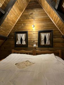 a bed in a wooden cabin with two windows at Vikendica Aview in Štrpce