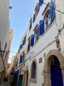 a white building with blue shutters on a street at Beau riad en médina, lumineux et avec terrasse privée sur mer in Essaouira