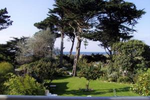 a garden with trees and green grass and the ocean at Holiday flat with sea and garden view, just 400m from the beach in Port-Blanc in Penvénan