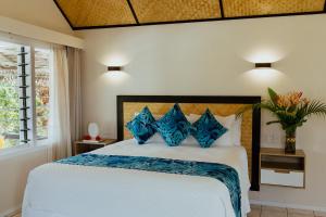 a bedroom with a large bed with blue pillows at Tai Roto Bay in Arutanga