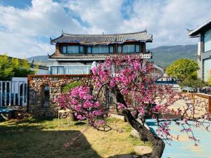 丽江玉龙白沙普宿客栈的一座建筑,前面有一棵树,上面有粉红色的花朵
