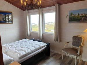a bedroom with a bed and a chair and two windows at Holiday home skudeneshavn III in Skudeneshavn