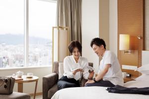 a man and woman sitting on a bed in a hotel room at Sheraton Grand Hiroshima Hotel in Hiroshima