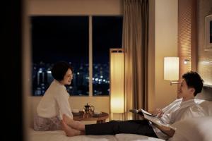 a woman talking to a man sitting on a bed in a hotel room at Sheraton Grand Hiroshima Hotel in Hiroshima