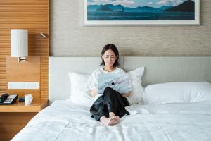 a woman sitting on a bed reading a magazine at Sheraton Grand Hiroshima Hotel in Hiroshima