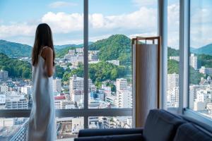 a woman in a white dress looking out of a window at Sheraton Grand Hiroshima Hotel in Hiroshima