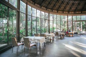 un restaurante con mesas, sillas y ventanas grandes en Treescape Resort Chiangmai, en Chiang Mai