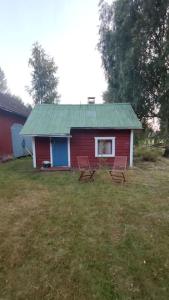 a red house with a green roof and two chairs at Mökki Kainula in Veteli