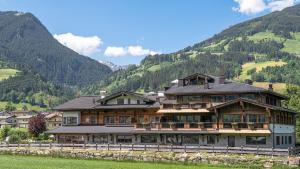 a large wooden house with mountains in the background at Aparthotel Stacherhof in Fügen