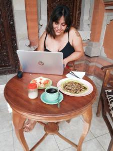 een vrouw aan een tafel met een laptop bij Tunjung Guest House in Ubud