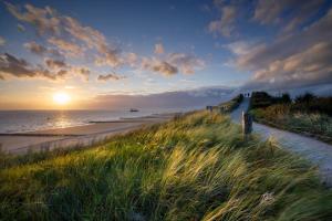 a beach with the sun setting on the water and grass at Luxe Kamer aan Zee in Zoutelande
