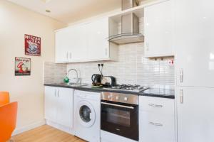 a kitchen with white cabinets and a washer and dryer at Comfortable Budget Apartment Next To Eurostar International - Kings Cross & Euston Station in London
