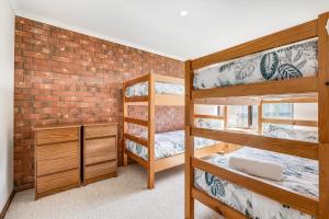 a room with three bunk beds and a brick wall at Beachfront Views at Southern Sands 1 in Port Elliot