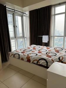 Fully furnished 1 BR Condo unit في مانيلا: غرفة نوم مع سرير مع لحاف ونوافذ