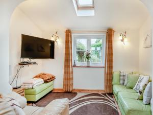 a living room with a green couch and a tv at Hare Cottage in North Tuddenham