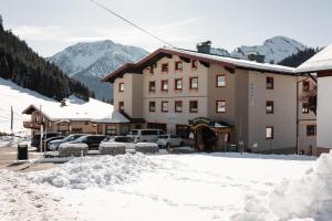 un hôtel dans la neige avec des voitures garées dans un parking dans l'établissement Hotel Rotlechhof, à Berwang