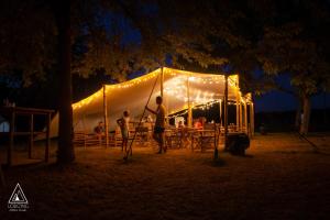 dos personas de pie delante de una tienda de campaña por la noche en Lodg'ing Nature Camp Châteaux de la Loire en Cellettes
