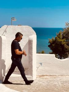 un hombre caminando por una pared blanca con el océano en Villa Olga studios, en Nea Skioni