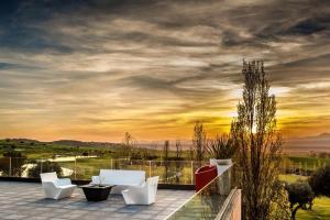 um pátio com cadeiras brancas e um pôr-do-sol ao fundo em Retamares Suites & Golf - a sólo 30 mn de Madrid - Vistas a los lagos y Montaña - Ven a descansar !! 