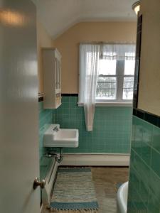 uma casa de banho em azulejo verde com um lavatório e uma janela em The Ashley em Saranac Lake