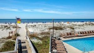 a swimming pool next to a beach with chairs and the ocean at Island Winds East by Brett Robinson Vacations in Gulf Shores