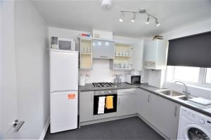 a white kitchen with a refrigerator and a sink at Spacious Two-Bedroom Apartment in Dagenham