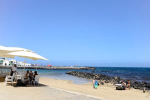 a group of people sitting on a beach with an umbrella at Apartamento Dunas De Famara in Famara