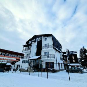 a white building with a black roof in the snow at Apartments and Rooms Ski in Vlasic