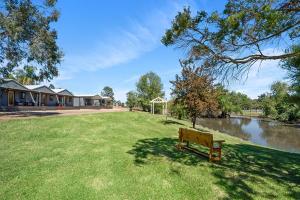 a park bench sitting in the grass next to a river at Horseshoe Tourist Park in Wagga Wagga