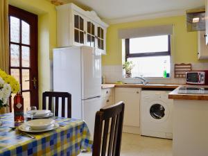 uma cozinha com uma mesa e um frigorífico branco em Violet Cottage em Llannon