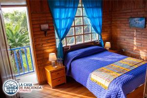 a bedroom with a bed with a blue comforter and a window at La Casa de Hacienda in Otavalo