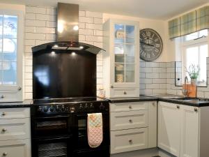 Raglan Cottage في Ardentinny: مطبخ مع موقد اسود مع ساعة على الحائط