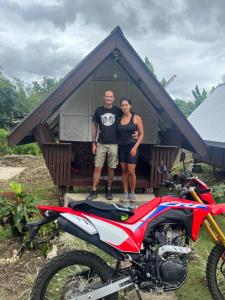 a man and woman standing in front of a house with a motorcycle at Roca's Homestay Backpackers Chalet in Batuan +7 photos