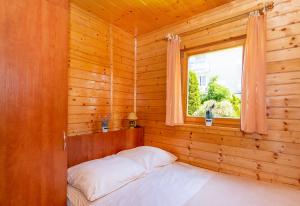 Cama en habitación de madera con ventana en Domki Letniskowe Patryk - 300m od plaży en Darlowko
