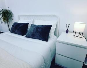 ein weißes Bett mit einem blauen Kissen und einem Nachttisch in der Unterkunft Glyfada Vacation Apt in Athen