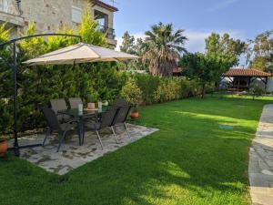 a table and chairs under an umbrella on a lawn at Villa Beta - 5min walk to beach, BBQ, Parking in Pefkohori +65 photos