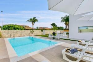 a swimming pool in a villa with white chairs at Domus Maulli - Villa sul mare in Marina di Ragusa