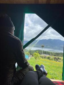 una persona sentada en una tienda mirando por la ventana en Refugio del Neusa, en Cogua