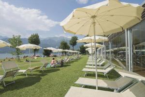 een rij witte stoelen en parasols op een strand bij Seven Park Hotel Lake Como - Adults Only in Colico