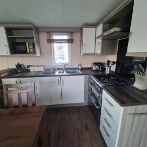 a kitchen with white cabinets and a stove top oven at Oscars caravan in Abergele