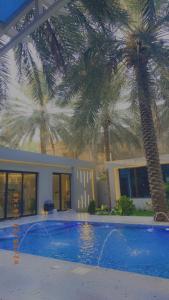 dos palmeras frente a una casa con piscina en لورينا شالية en Al Hofuf