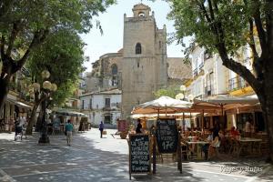 una calle con mesas y sombrillas y una torre de reloj en Casa Palacio Arcos del Carmen, en Jerez de la Frontera