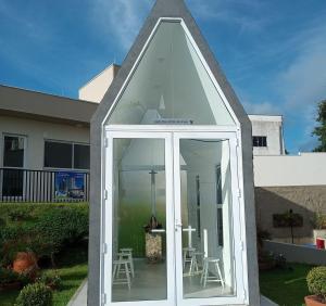 ein spitzbogiger Wintergarten mit weißen Türen und Stühlen vor einem Haus in der Unterkunft Condomínio da fé Canção Nova Com Garagem in Cachoeira Paulista